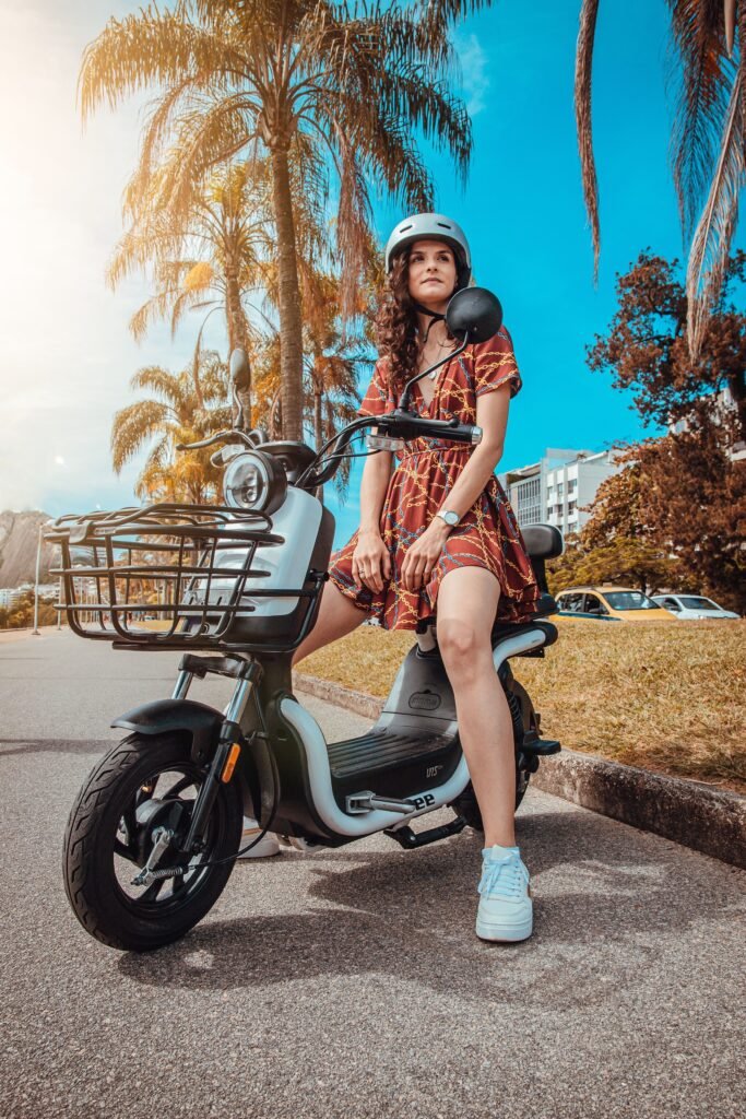 Young woman in a patterned dress and helmet sitting on an electric scooter on a sunny day.