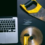 Flat lay of a laptop and various hand tools on a dark surface, perfect for DIY or technology themes.